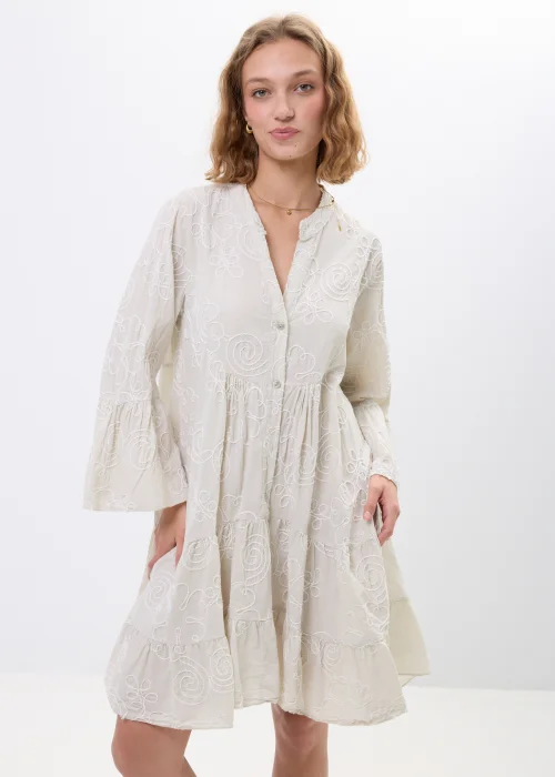 Beżowa sukienka boho z subtelnym haftowanym wzorem spiral i kwiatowych motywów. Zwiewny fason z falbanami, dekoltem V oraz rozszerzanymi rękawami pięknie układa się na sylwetce, nadając stylizacji lekkości i romantycznego charakteru.