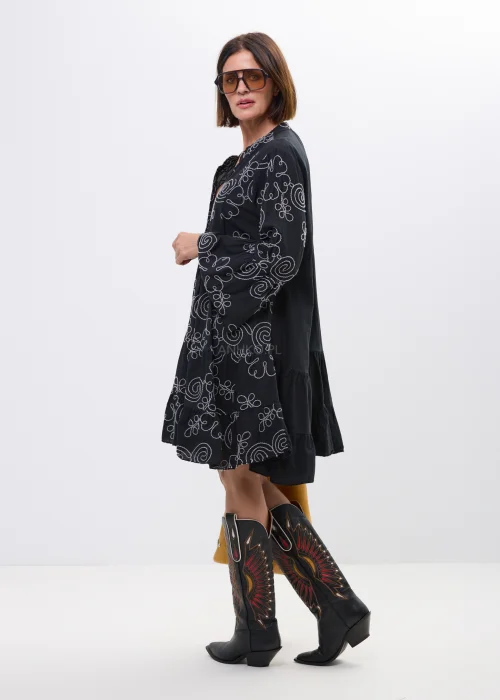 Czarna sukienka boho z białym haftowanym wzorem spiral i kwiatowych ornamentów. Rozkloszowany fason z falbaną, długimi rozszerzanymi rękawami i dekoltem V.