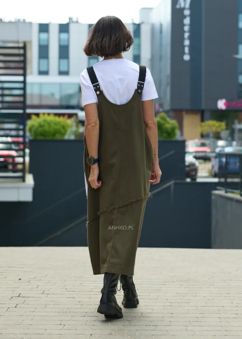 Khaki sukienka ogrodniczka midi z regulowanymi szelkami i kontrastową kieszenią z nadrukiem. Casualowy model o luźnym fasonie, zestawiony z białym T-shirtem i czarnymi botkami.