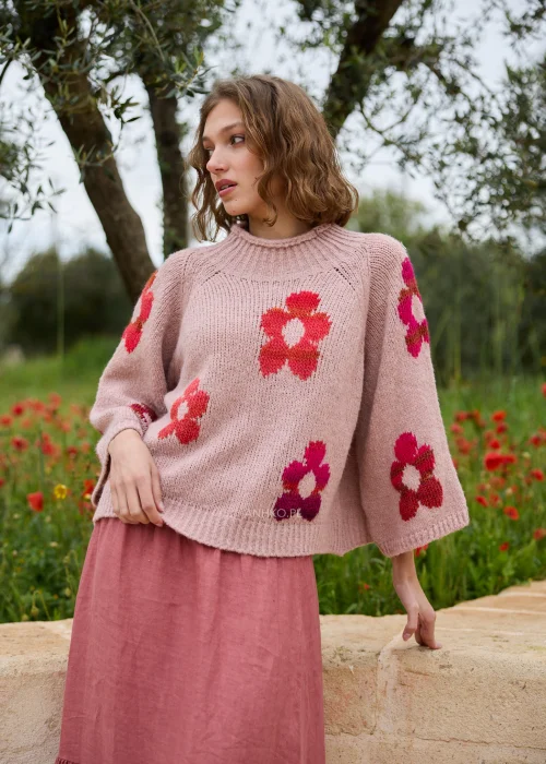 Sweter pudroworóżowy z kolorowym motywem kwiatów w odcieniach różu, czerwieni i fuksji. Miękki fason z szerokimi rękawami dodaje stylizacji przytulnego, kobiecego charakteru