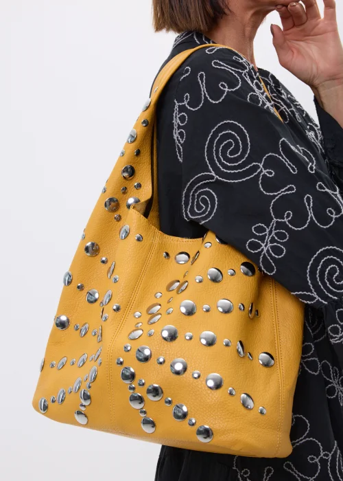 Musztardowa torebka shopper zdobiona srebrnymi nitami o różnych rozmiarach. Duży model na ramię z efektownymi metalicznymi detalami w rockowym stylu.