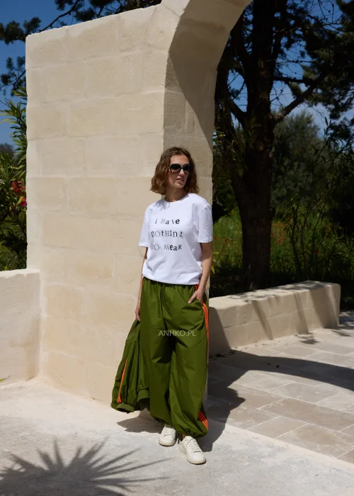 Biały T-shirt damski z nadrukiem „I Have Nothing To Wear” w czarnym kolorze. Luźny model casual zestawiony z zielonymi spodniami i okularami przeciwsłonecznymi.