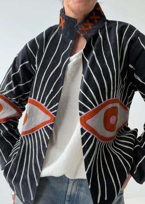 Żakiet damski w kolorze czarnym z efektownym haftem oka oraz promienistymi liniami w kontrastowym jasnym kolorze. Oryginalny model o artystycznym charakterze inspirowany symboliką „evil eye”.