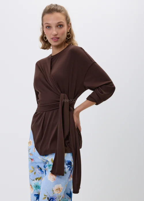 Brązowa bluzka z efektownym wiązaniem w talii i luźnym fasonem oversize. Model z długim rękawem oraz asymetrycznym drapowaniem podkreśla sylwetkę i tworzy elegancką, kobiecą stylizację.