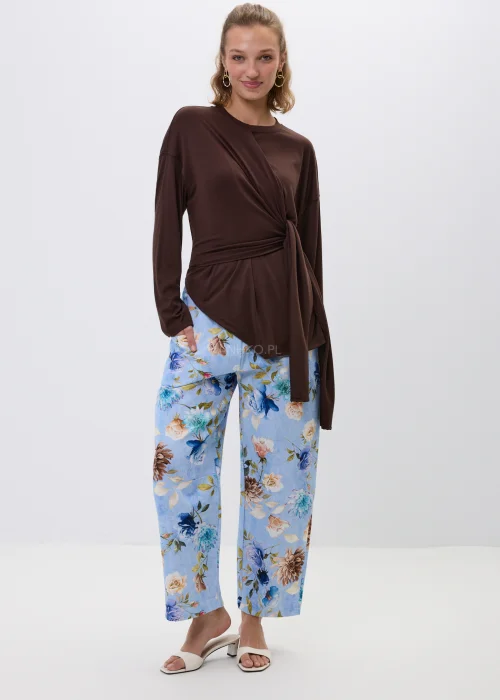 Brązowa bluzka z efektownym wiązaniem w talii i luźnym fasonem oversize. Model z długim rękawem oraz asymetrycznym drapowaniem podkreśla sylwetkę i tworzy elegancką, kobiecą stylizację.