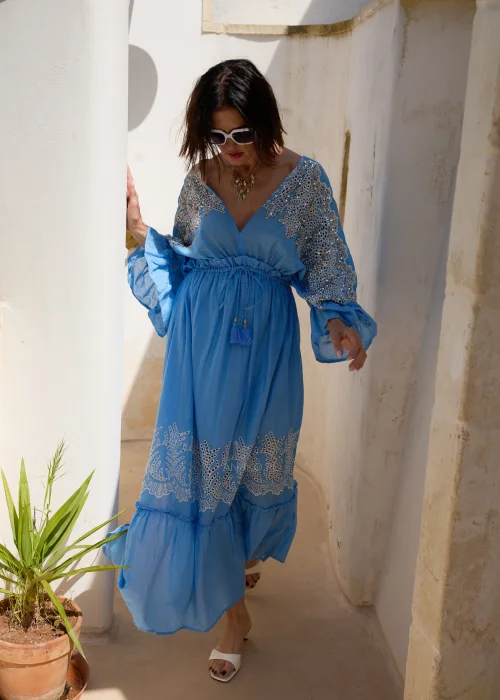 Błękitna sukienka maxi w stylu boho z koronkowymi zdobieniami, dekoltem V i wiązaniem w talii z chwostami. Zwiewny model z szerokimi rękawami, idealny do wakacyjnych i eleganckich stylizacji.