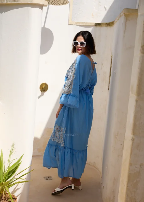 Błękitna sukienka maxi w stylu boho z koronkowymi zdobieniami, dekoltem V i wiązaniem w talii z chwostami. Zwiewny model z szerokimi rękawami, idealny do wakacyjnych i eleganckich stylizacji.