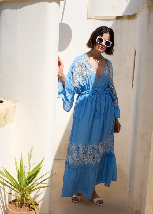 Błękitna sukienka maxi w stylu boho z koronkowymi zdobieniami, dekoltem V i wiązaniem w talii z chwostami. Zwiewny model z szerokimi rękawami, idealny do wakacyjnych i eleganckich stylizacji.
