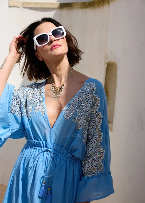 Błękitna sukienka maxi w stylu boho z koronkowymi zdobieniami, dekoltem V i wiązaniem w talii z chwostami. Zwiewny model z szerokimi rękawami, idealny do wakacyjnych i eleganckich stylizacji.