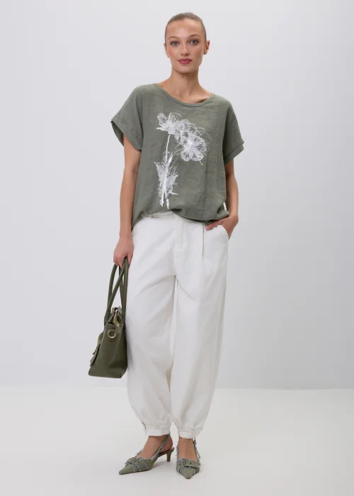 Oliwkowy damski T-shirt oversize z białym kwiatowym nadrukiem i podwijanymi rękawami. Luźna bluzka w naturalnym stylu, zestawiona z białymi szerokimi spodniami i torebką, idealna do codziennych stylizacji.