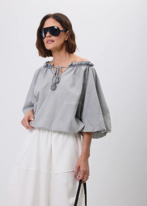 Szara bluzka damska o luźnym fasonie z bufiastymi rękawami i wiązaniem przy dekolcie zakończonym chwostami. Lekki model w stylu boho, idealny do spódnic i spodni w codziennych oraz eleganckich stylizacjach.