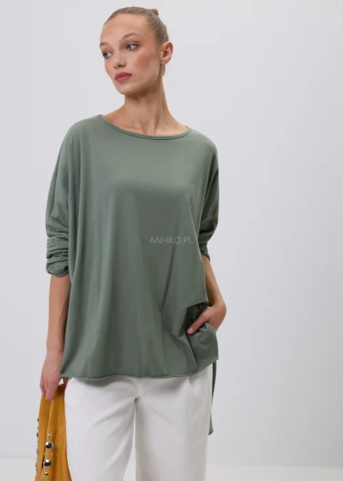 Oliwkowa damska bluzka oversize z długim rękawem i asymetrycznym dołem, wykonana z miękkiej dzianiny. Minimalistyczna stylizacja casual z białymi spodniami, idealna na co dzień i do nowoczesnych zestawów.