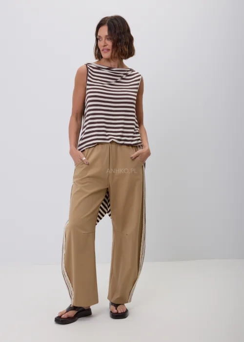 Damski top bez rękawów w beżowo-brązowe paski o luźnym, asymetrycznym fasonie. Modna stylizacja casual ze spodniami w kolorze camel z ozdobnym koronkowym lampasem, inspirowana naturalną elegancją.