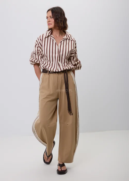 Damska koszula w beżowo-brązowe pionowe paski z kołnierzykiem i podwijanymi rękawami. Elegancka stylizacja casual ze spodniami w odcieniu camel i ozdobnym plecionym paskiem.