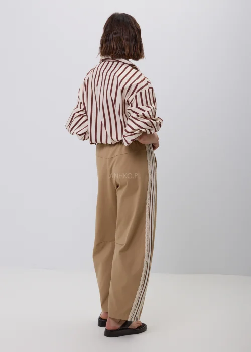 Damska koszula w beżowo-brązowe pionowe paski z kołnierzykiem i podwijanymi rękawami. Elegancka stylizacja casual ze spodniami w odcieniu camel i ozdobnym plecionym paskiem.