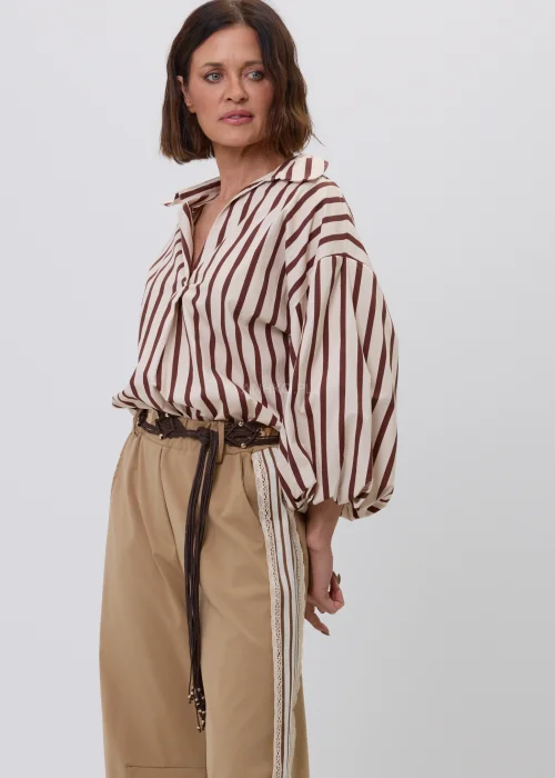 Damska koszula w beżowo-brązowe pionowe paski z kołnierzykiem i podwijanymi rękawami. Elegancka stylizacja casual ze spodniami w odcieniu camel i ozdobnym plecionym paskiem.