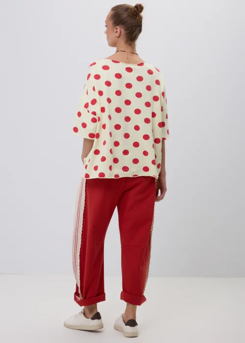 Kremowa damska bluzka oversize w czerwone grochy z rękawem 3/4, zestawiona z czerwonymi spodniami z koronkowym lampasem. Modna stylizacja casual inspirowana stylem retro i francuską elegancją.