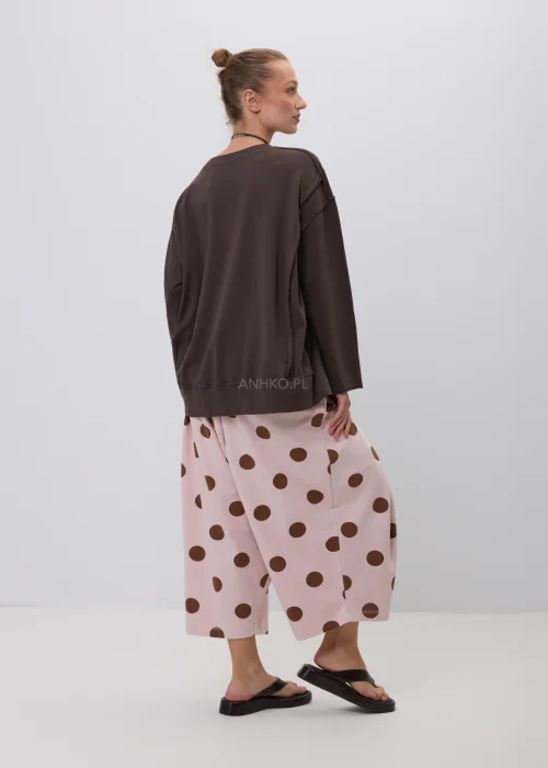 Brązowa bluza damska oversize z długim rękawem i okrągłym dekoltem, o swobodnym fasonie z ozdobnymi przeszyciami. Casualowa stylizacja z szerokimi spodniami w grochy podkreśla wygodny i nowoczesny charakter modelu.