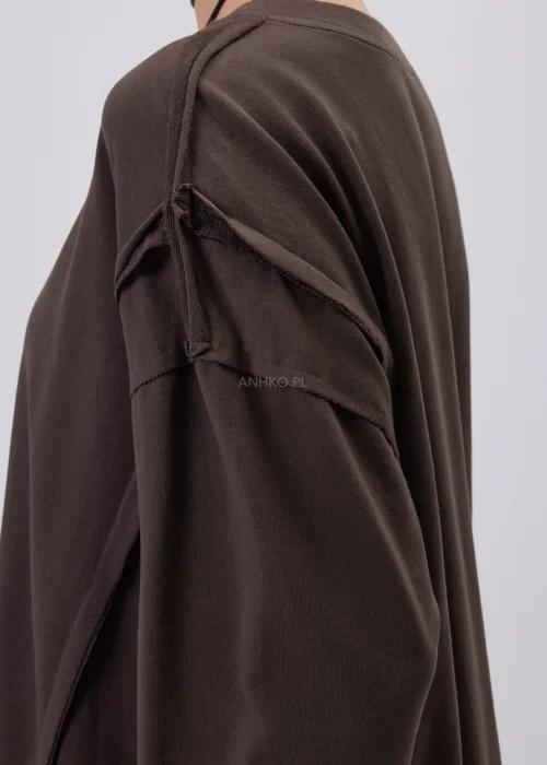 Brązowa bluza damska oversize z długim rękawem i okrągłym dekoltem, o swobodnym fasonie z ozdobnymi przeszyciami. Casualowa stylizacja z szerokimi spodniami w grochy podkreśla wygodny i nowoczesny charakter modelu.