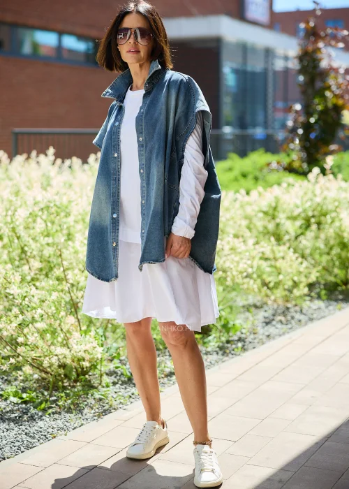 Jeansowa kamizelka oversize damska z efektem sprania, zapinana na napy, z szerokimi rękawami i wysokim kołnierzem. Model stylizowany z białą sukienką, tworzący nowoczesny casualowy look.
