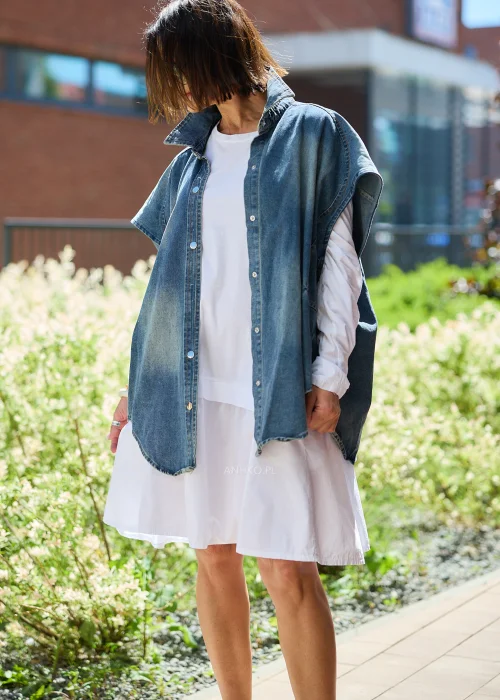 Jeansowa kamizelka oversize damska z efektem sprania, zapinana na napy, z szerokimi rękawami i wysokim kołnierzem. Model stylizowany z białą sukienką, tworzący nowoczesny casualowy look.