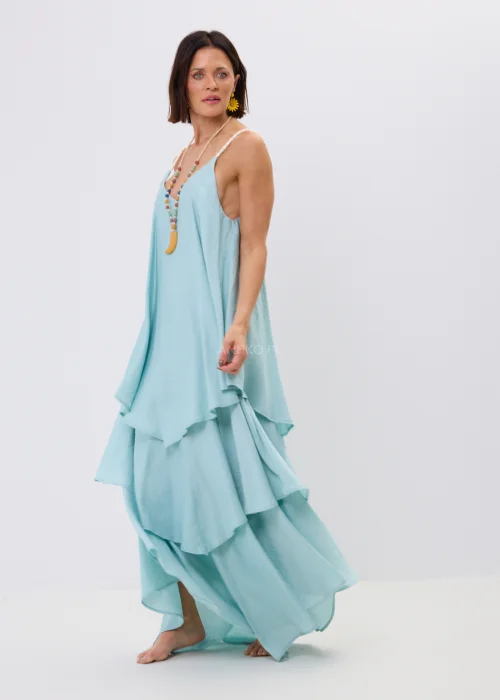 Błękitna sukienka maxi damska na cienkich ramiączkach z ozdobnym splotem, o luźnym fasonie i wielowarstwowych falbanach. Zwiewny model w stylu boho uzupełniony kolorowym naszyjnikiem i letnimi dodatkami.