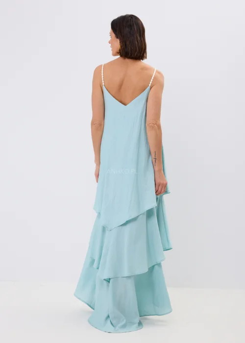 Błękitna sukienka maxi damska na cienkich ramiączkach z ozdobnym splotem, o luźnym fasonie i wielowarstwowych falbanach. Zwiewny model w stylu boho uzupełniony kolorowym naszyjnikiem i letnimi dodatkami.