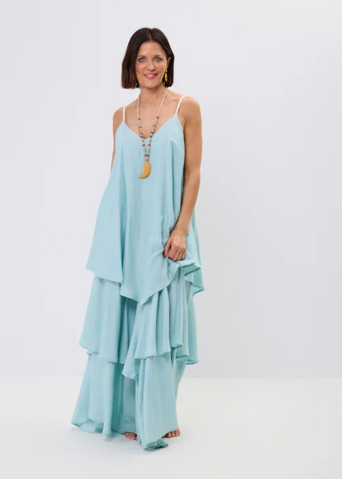 Błękitna sukienka maxi damska na cienkich ramiączkach z ozdobnym splotem, o luźnym fasonie i wielowarstwowych falbanach. Zwiewny model w stylu boho uzupełniony kolorowym naszyjnikiem i letnimi dodatkami.