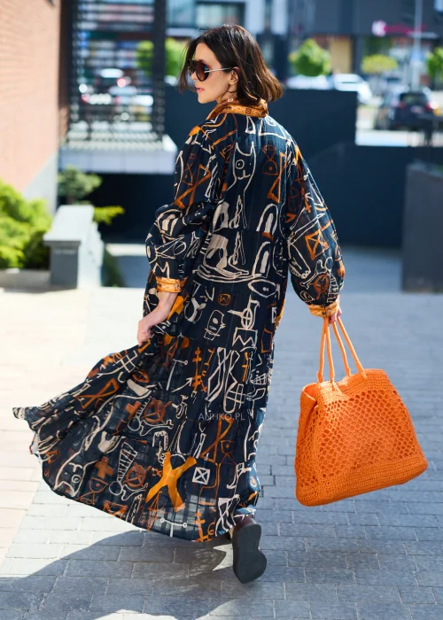 Pomarańczowa ażurowa torebka shopper wykonana z plecionego splotu z krótkimi uchwytami. Lekki, pojemny model doskonale uzupełnia letnią stylizację z czarną sukienką we wzory w odcieniach pomarańczu i beżu.
