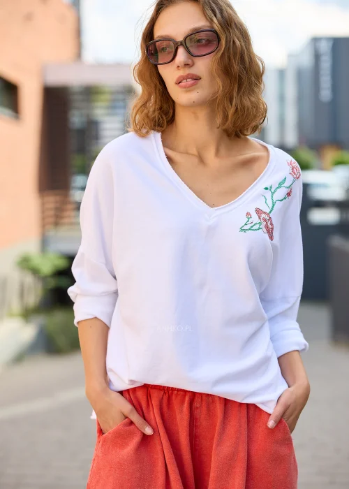 Biała bluzka damska Scarlet Bloom z dekoltem V i haftem kwiatowym przy dekolcie, luźny fason z opuszczoną linią ramion, styl casual.