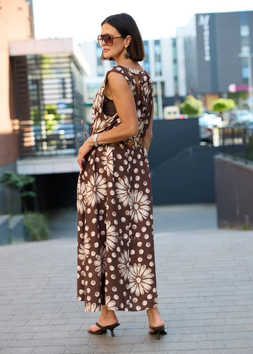 Sukienka maxi Plus Size w brązowym kolorze z dużym kwiatowym wzorem i białymi groszkami, z okrągłym dekoltem, kieszeniami i ozdobnym paskiem w talii, prezentowana w miejskiej stylizacji.