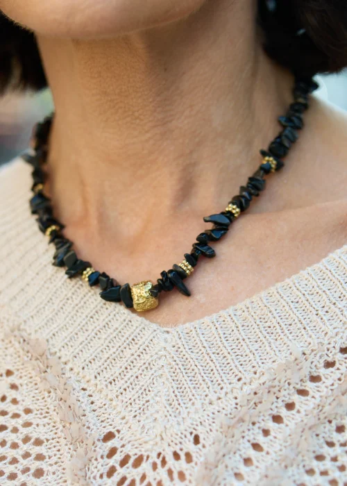Czarny naszyjnik z naturalnego onyksu wykonany z nieregularnych bryłek kamienia i ozdobnych złotych detali. Biżuteria w stylu boho z regulowanym zapięciem ze stali nierdzewnej.
