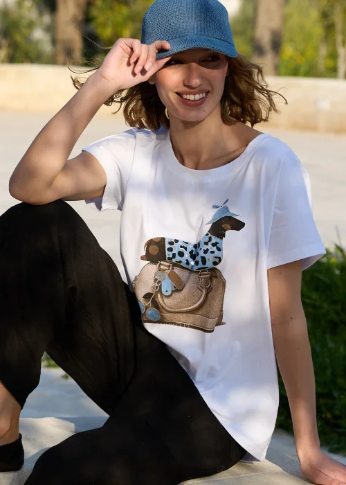 Biały damski T-shirt z kolorowym nadrukiem jamnika w niebieskiej czapce siedzącego na torebce. Luźny fason z krótkim rękawem doskonale komponuje się z czarnymi lnianymi spodniami i codziennymi stylizacjami.