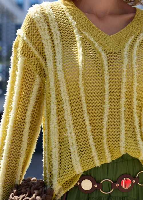 Ażurowy sweter o luźnym fasonie oversize z dekoltem w serek (V) oraz długimi rękawami. Model wykonany z lekkiego, dekoracyjnego splotu z pionowymi, wypukłymi pasami, zakończony ściągaczami przy dekolcie