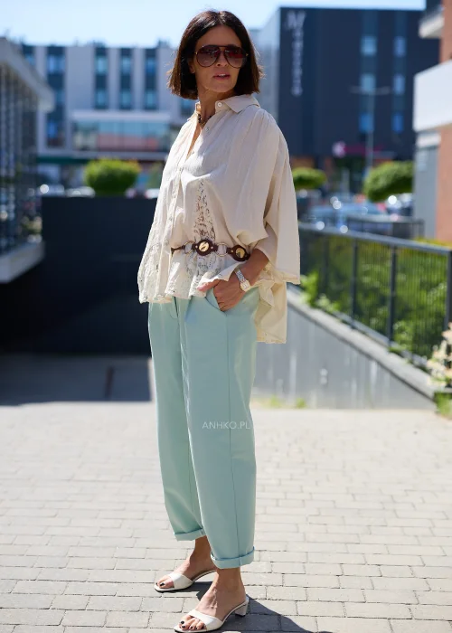 Biała oversize bluzka z koronkowym dołem i szerokimi rękawami, zapinana na guziki, zestawiona z miętowymi spodniami w lekkiej eleganckiej stylizacji
