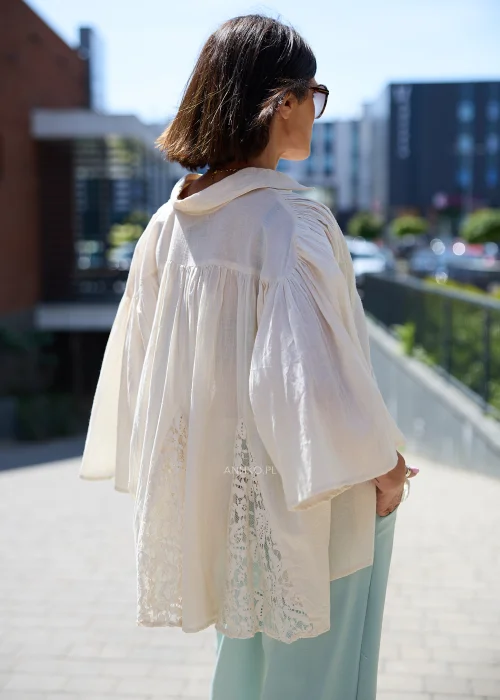 Biała oversize bluzka z koronkowym dołem i szerokimi rękawami, zapinana na guziki, zestawiona z miętowymi spodniami w lekkiej eleganckiej stylizacji