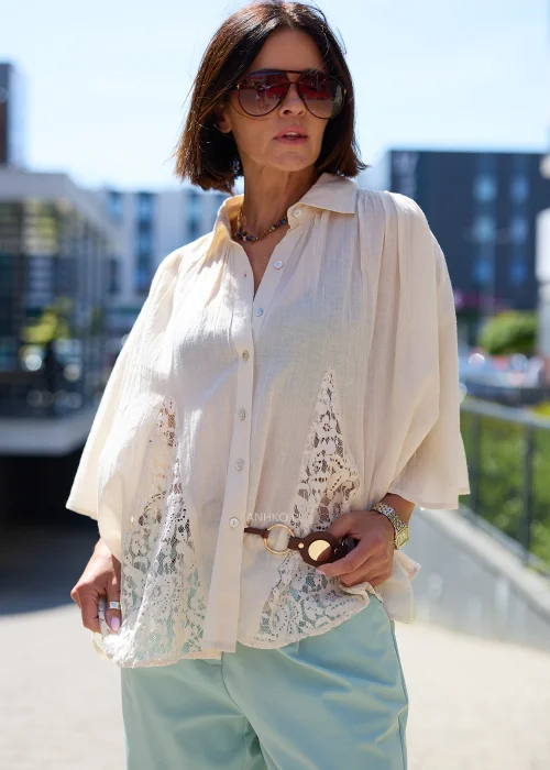 Biała oversize bluzka z koronkowym dołem i szerokimi rękawami, zapinana na guziki, zestawiona z miętowymi spodniami w lekkiej eleganckiej stylizacji