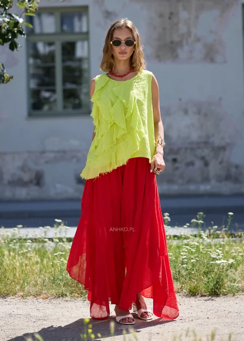Czerwone szerokie spodnie maxi z asymetrycznymi panelami i zwiewnej tkaniny, zestawione z luźną bluzką oraz ozdobnym paskiem w stylu boho.