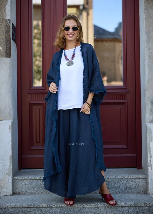 Granatowe lniane kimono damskie z szerokimi rękawami i surowym wykończeniem, narzucone na białą bluzkę i szerokie spodnie w eleganckiej stylizacji