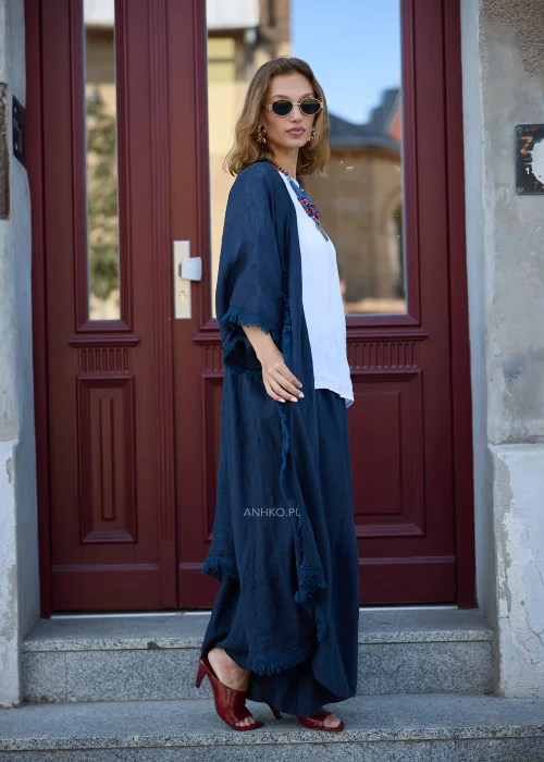 Granatowe lniane kimono damskie z szerokimi rękawami i surowym wykończeniem, narzucone na białą bluzkę i szerokie spodnie w eleganckiej stylizacji