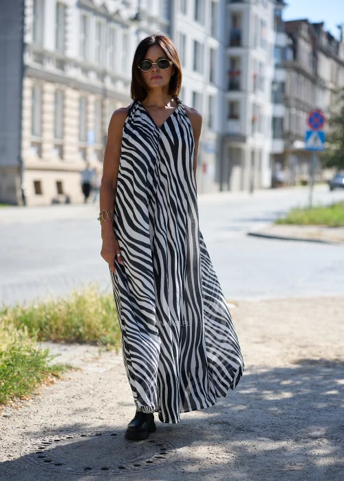 Sukienka maxi z luźnym, rozszerzanym fasonem, stójką z dekoltem V oraz wiązaniem przy szyi. Model bez rękawów, wykonany z lekkiego materiału