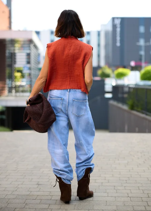 Ceglana lniana kamizelka damska z ozdobnymi guzikami i stójką, zestawiona z jasnymi jeansami w casualowej stylizacji z biżuterią